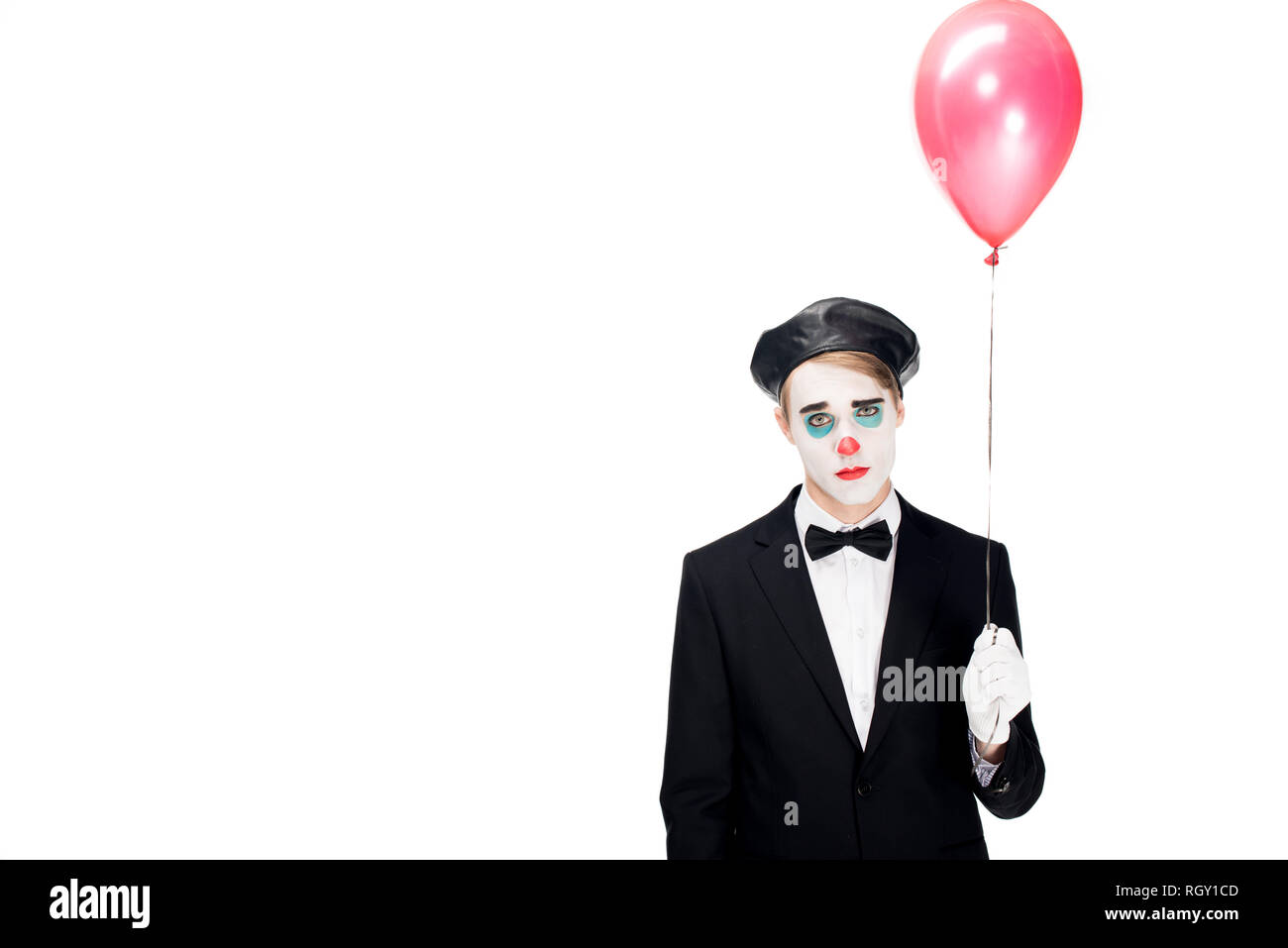 Sconvolto clown in tuta e berretto nero tenendo il palloncino e in piedi isolato su bianco Foto Stock