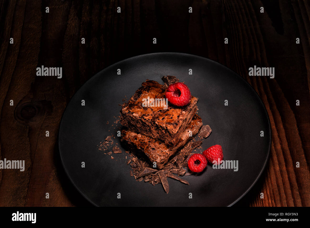 Il lampone e due i biscotti su una piastra nera con scaglie di cioccolato scuro sulla tavola di legno. Formato orizzontale con copia spazio. Foto Stock