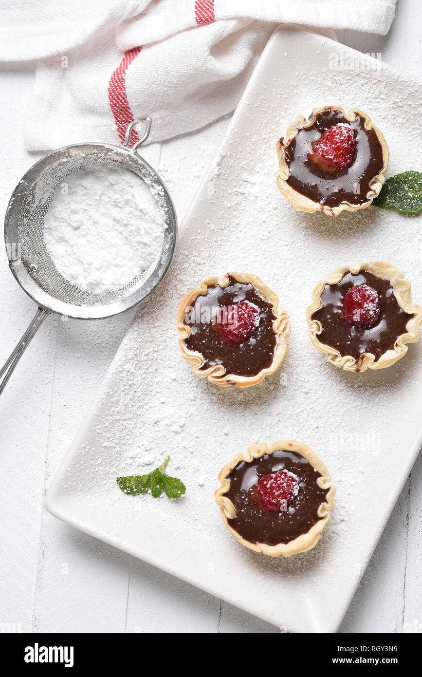 Mousse al cioccolato in pasticceria gusci con lamponi e zucchero a velo. Foto Stock