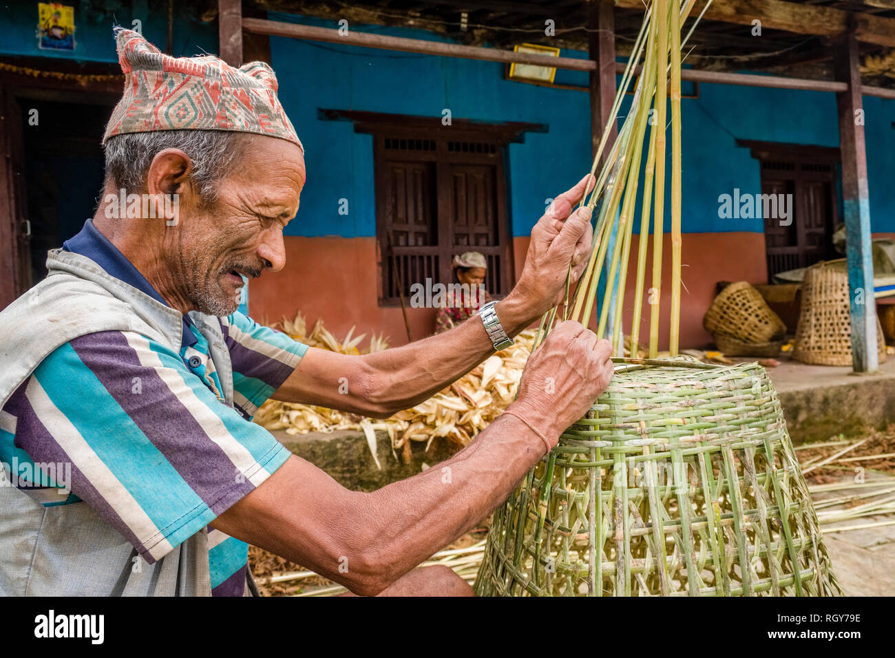Locale calza uomo un cestello, sua moglie raccolta mais dietro di lui a casa sua Foto Stock
