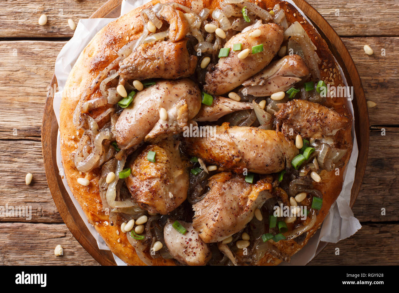 Piatto palestinese di pollo con sommaco, i pinoli e le cipolle su un pane piatto closeup sul tavolo. parte superiore orizzontale vista da sopra Foto Stock