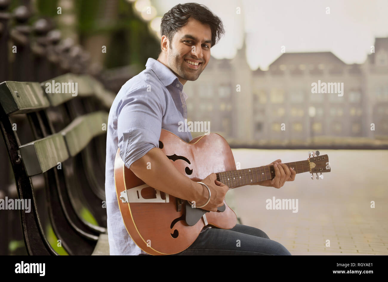 Giovane uomo seduto su un banco da lavoro e suonare la chitarra all'aperto Foto Stock