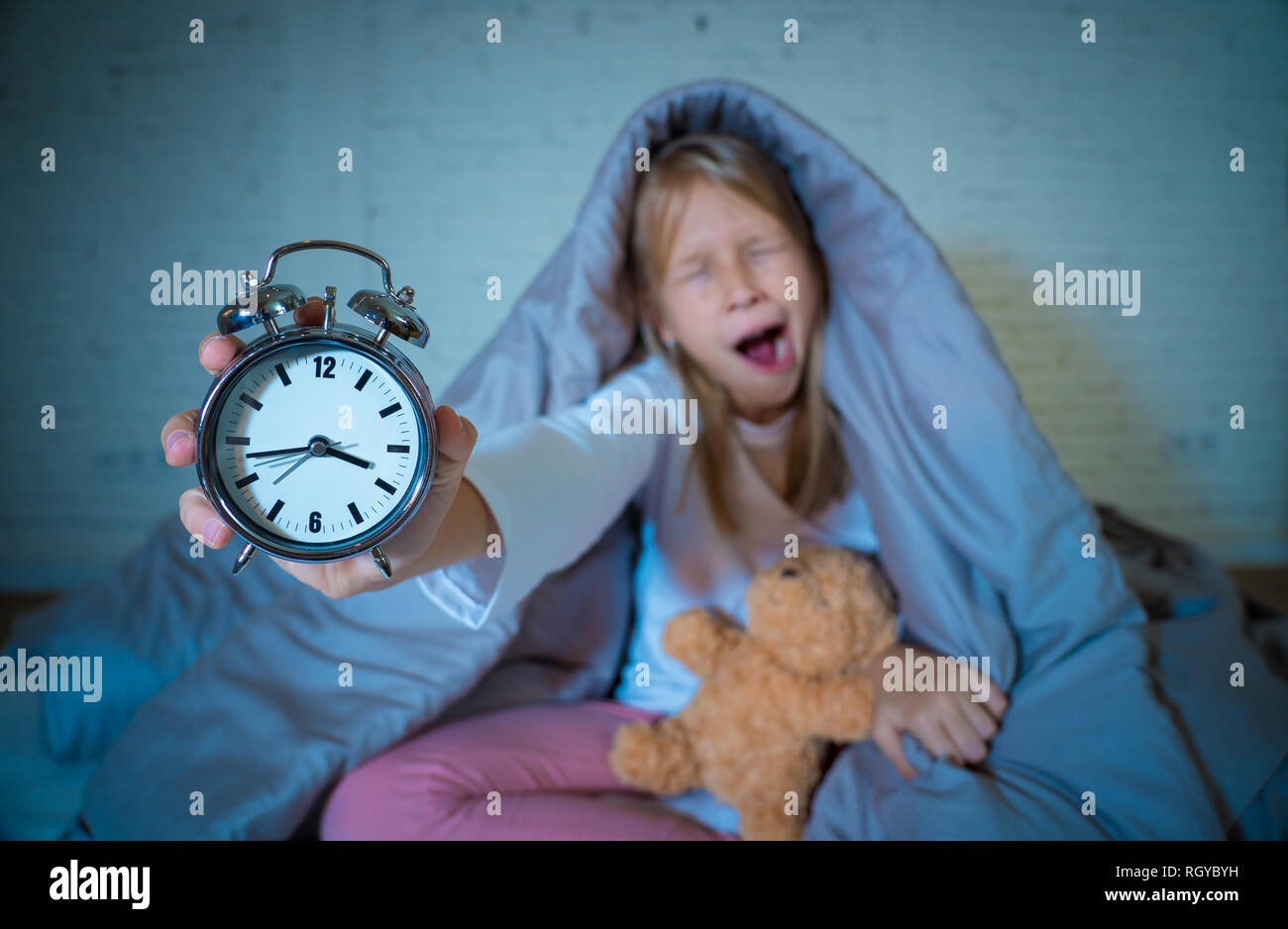 Carino piccolo insonni ragazza seduta sul letto che mostra orologio sveglia cercando stanco aventi disturbi del sonno soggiorno addormentato durante la notte o alla riattivazione troppo presto in ch Foto Stock