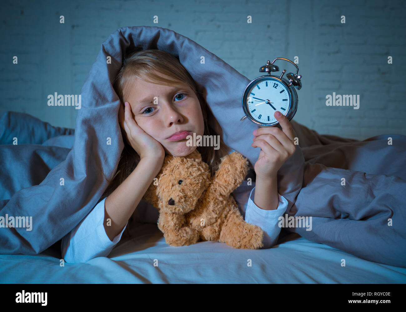 Carino insonne bambina giacente nel letto che mostra orologio sveglia cercando stanco aventi disturbi del sonno soggiorno addormentato durante la notte o alla riattivazione troppo presto in Chil Foto Stock