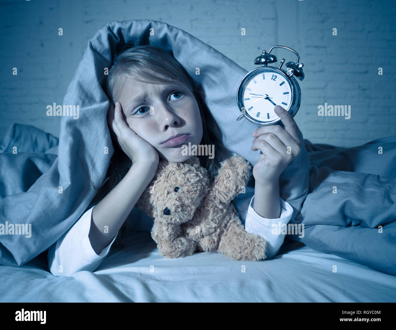 Carino insonne bambina giacente nel letto che mostra orologio sveglia cercando stanco aventi disturbi del sonno soggiorno addormentato durante la notte o alla riattivazione troppo presto in Chil Foto Stock