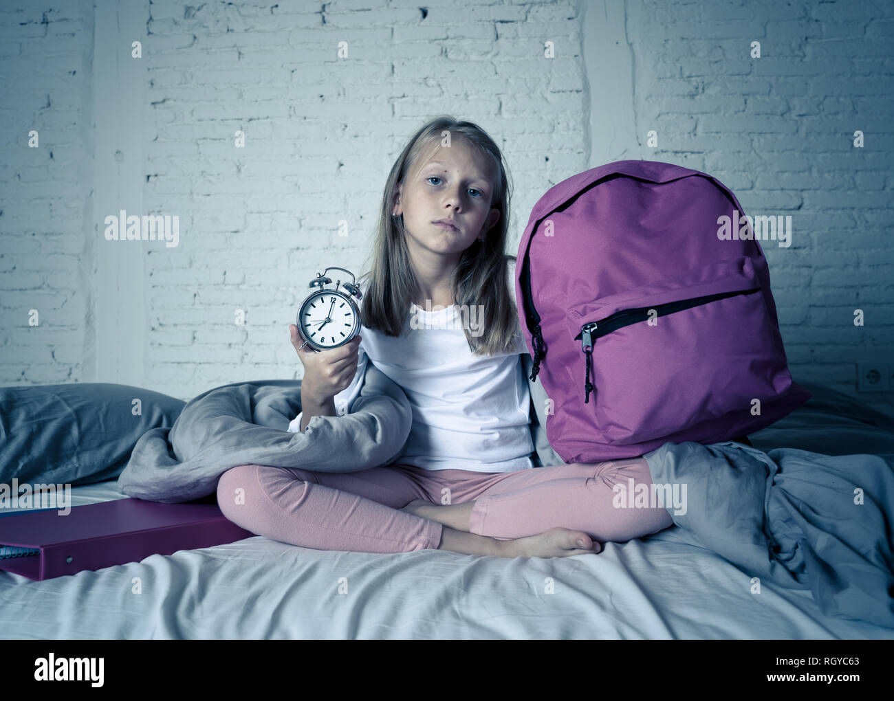 Bella bionda bambina triste e insonni arrabbiato che mostra orologio sveglia tempo di prepararsi per la scuola in difficoltà di svegliarvi al mattino bambini Foto Stock