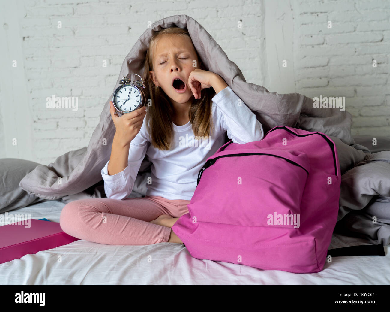 Bella bionda bambina triste e insonni arrabbiato che mostra orologio sveglia tempo di prepararsi per la scuola in difficoltà di svegliarvi al mattino bambini Foto Stock