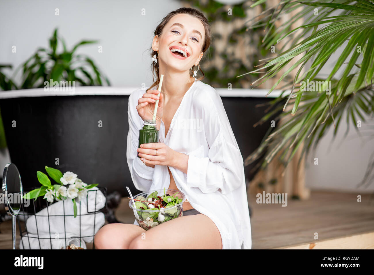 Bella donna frullato di bere durante la seduta con una sana insalata in bagno. Mangiare sano e concetto di bellezza Foto Stock