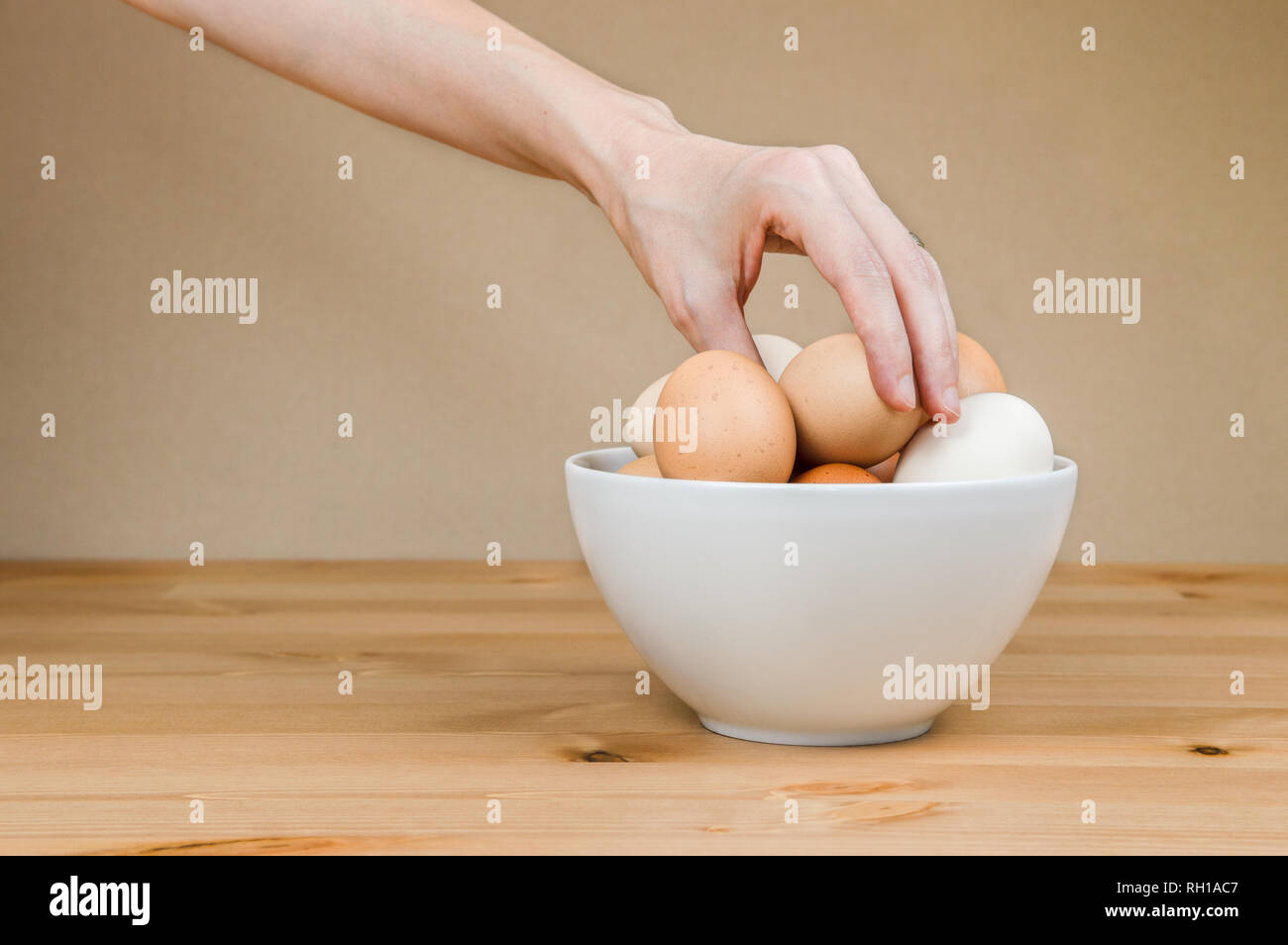 Mano femminile prendendo un uovo dal bianco ciotola su una tavola . Foto Stock