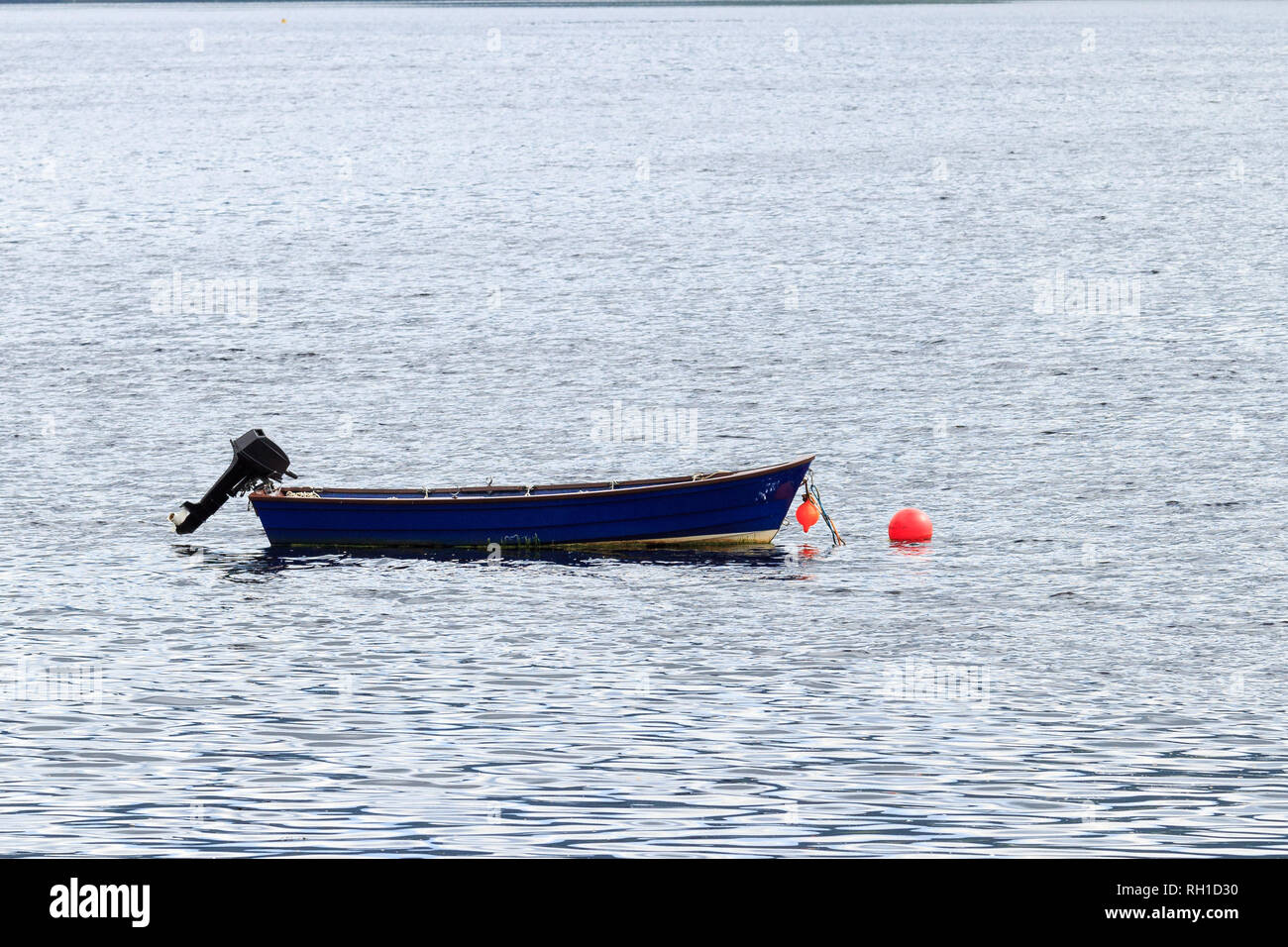 Piccola barca a remi con motore fuoribordo ormeggiata in un scozzese Loch Foto Stock