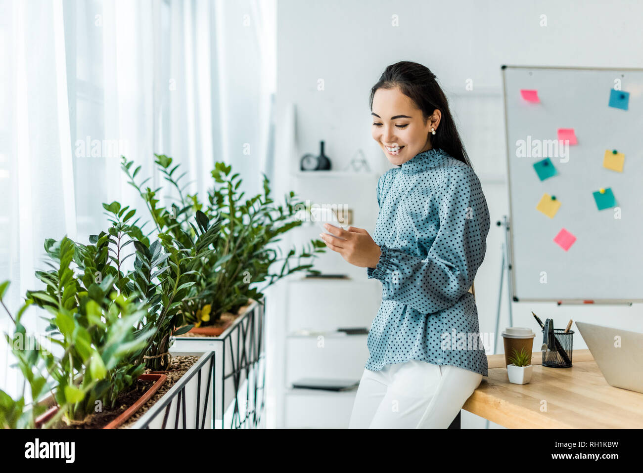 Bella sorridente asian imprenditrice utilizza lo smartphone in office Foto Stock