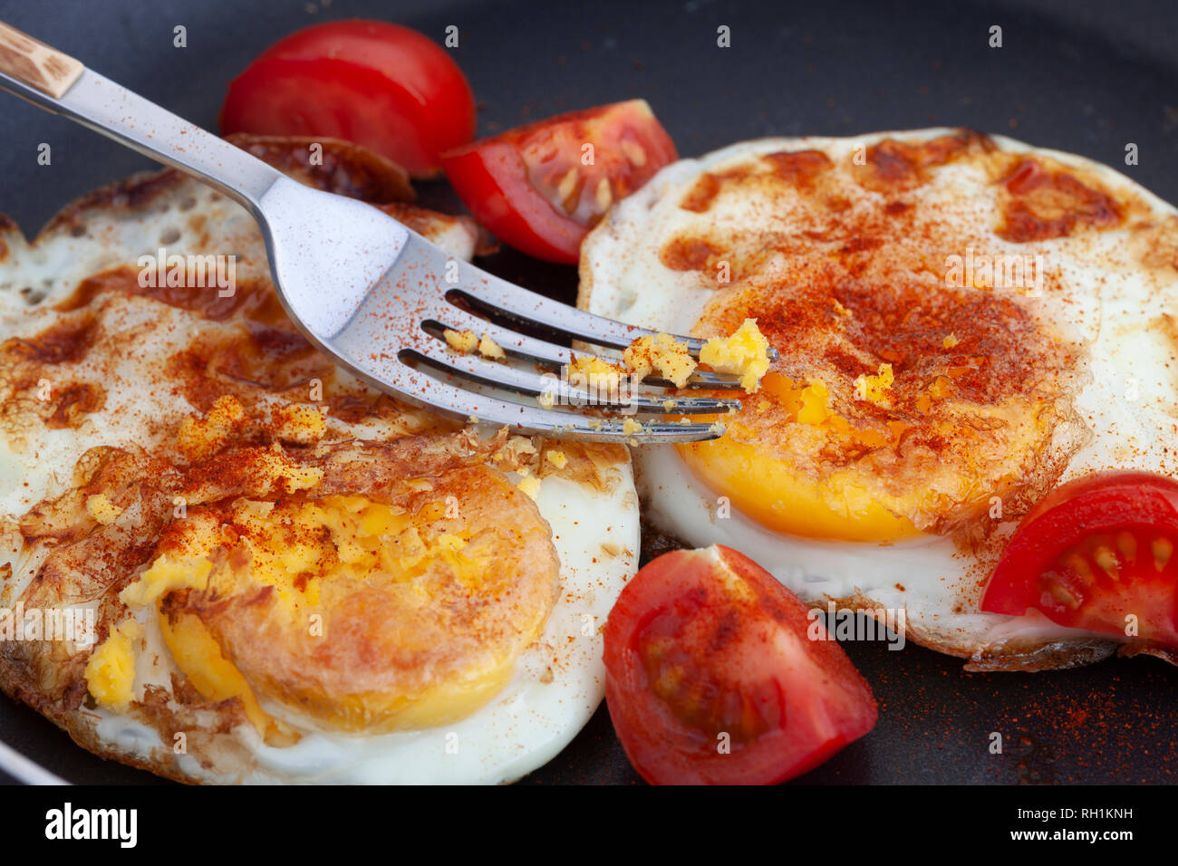 Uova fritte in padella con la paprica affumicata e pomodori ciliegini. Illuminazione naturale. Close up. Foto Stock