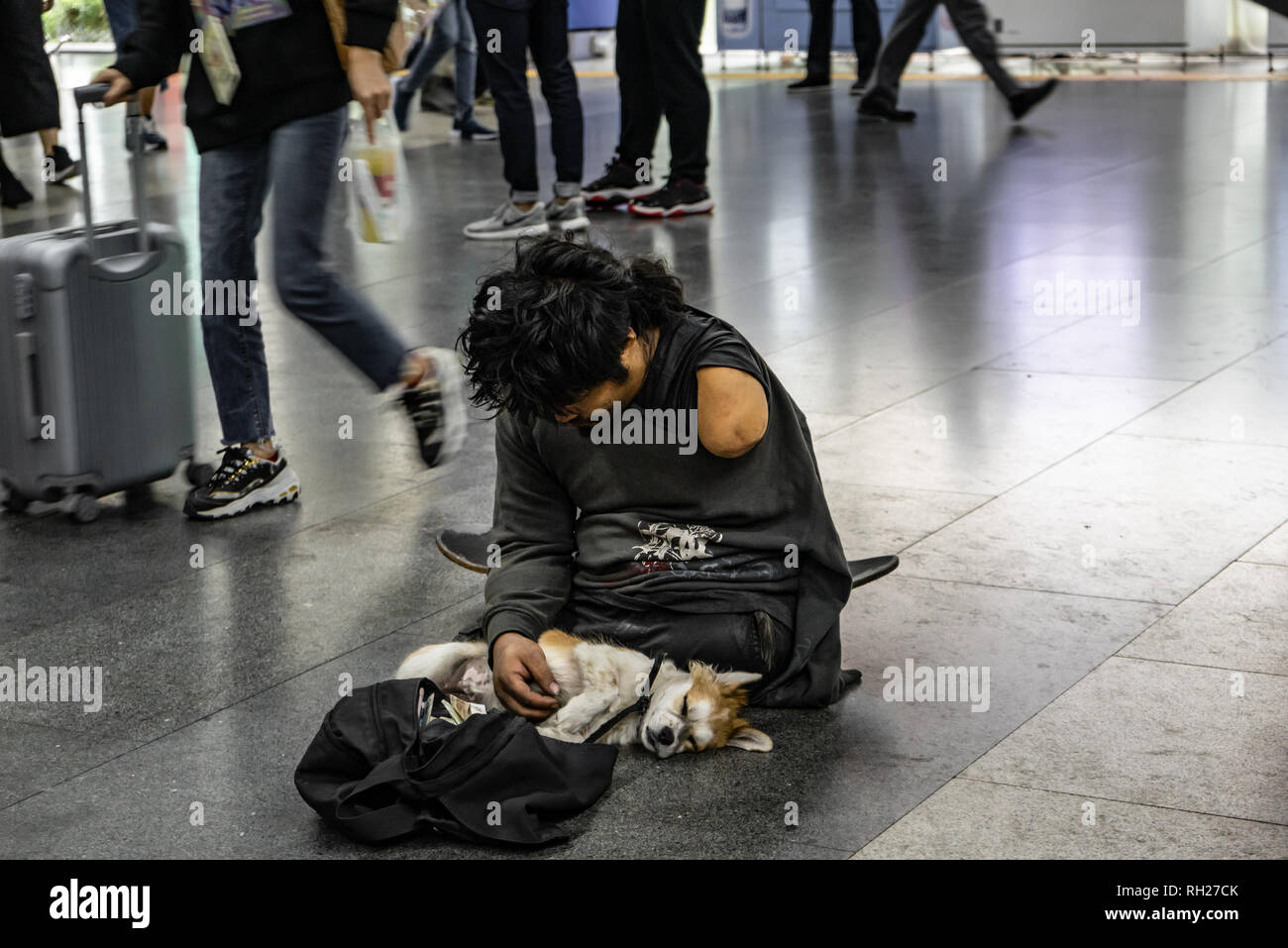 Senzatetto uomo con braccio mancante e il suo cane in uno spazio pubblico di Shenzhen, Cina Foto Stock