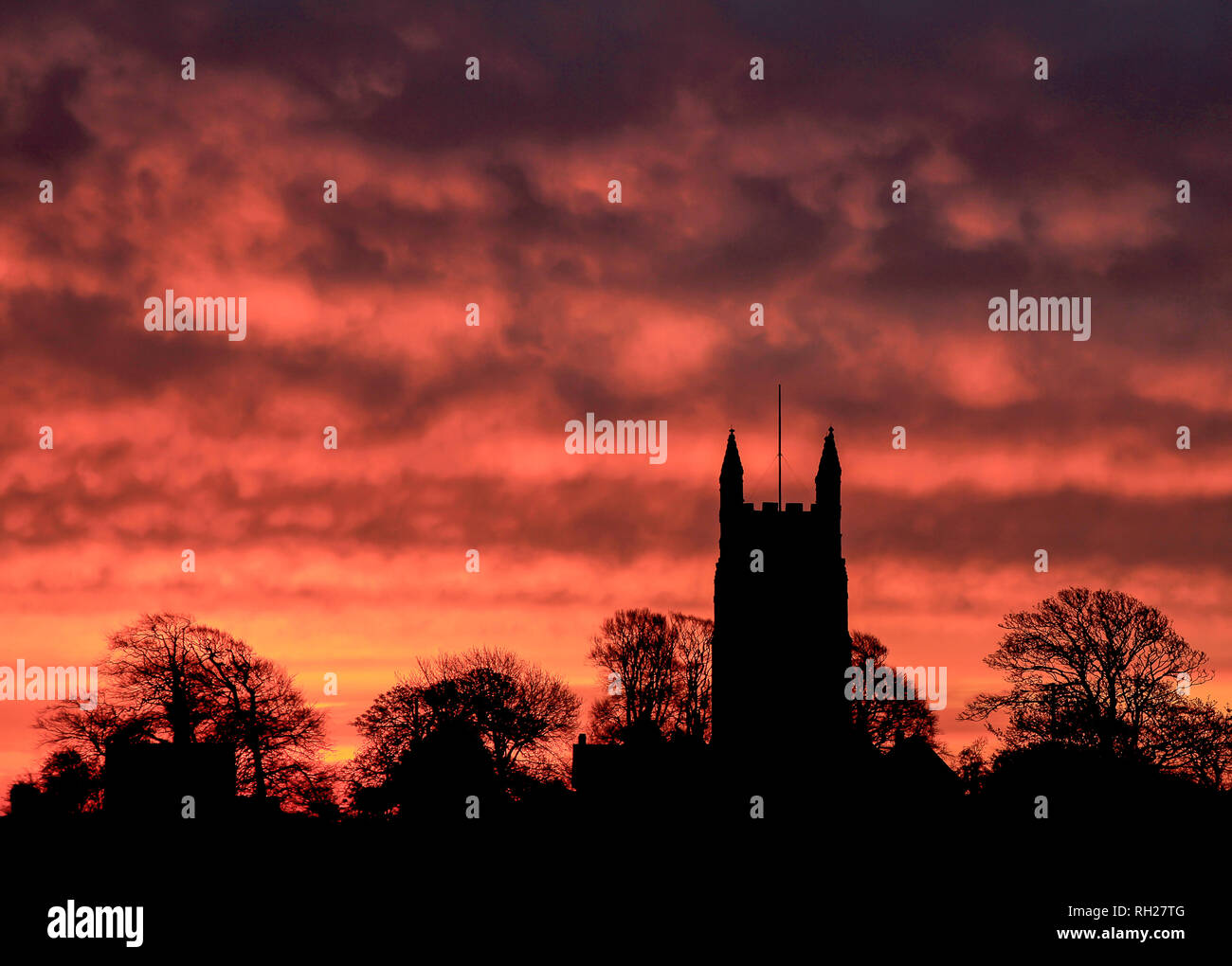 Fiery Sunset, Maker Chiesa, Mount Edgecumbe, Cornwall. Alberi e chiesa profilarsi nel bagliore di mattina. Foto Stock