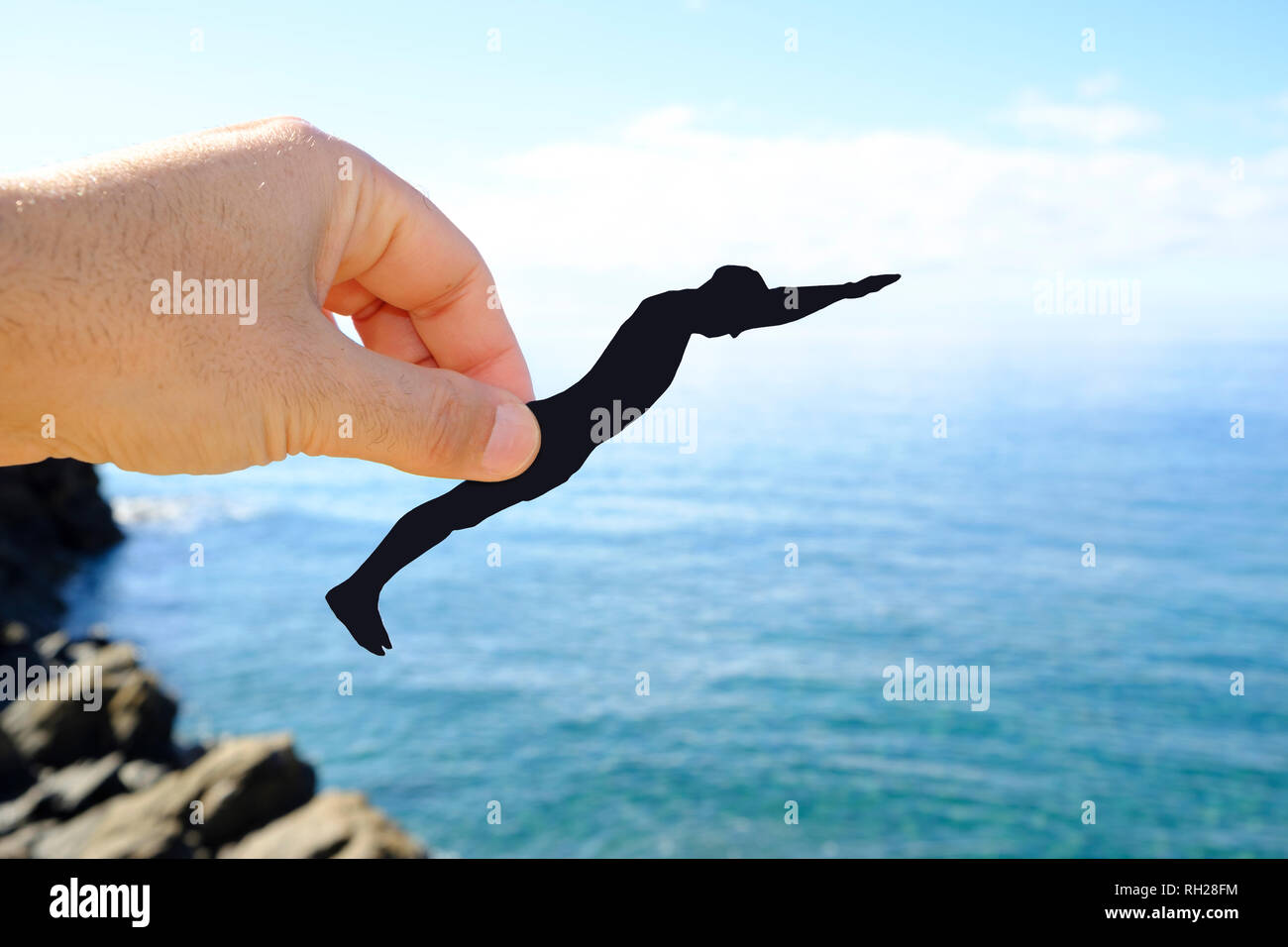 Primo piano della mano di un uomo nero con un ritaglio di carta nella forma di un uomo che sta per gettarsi nell'oceano Foto Stock