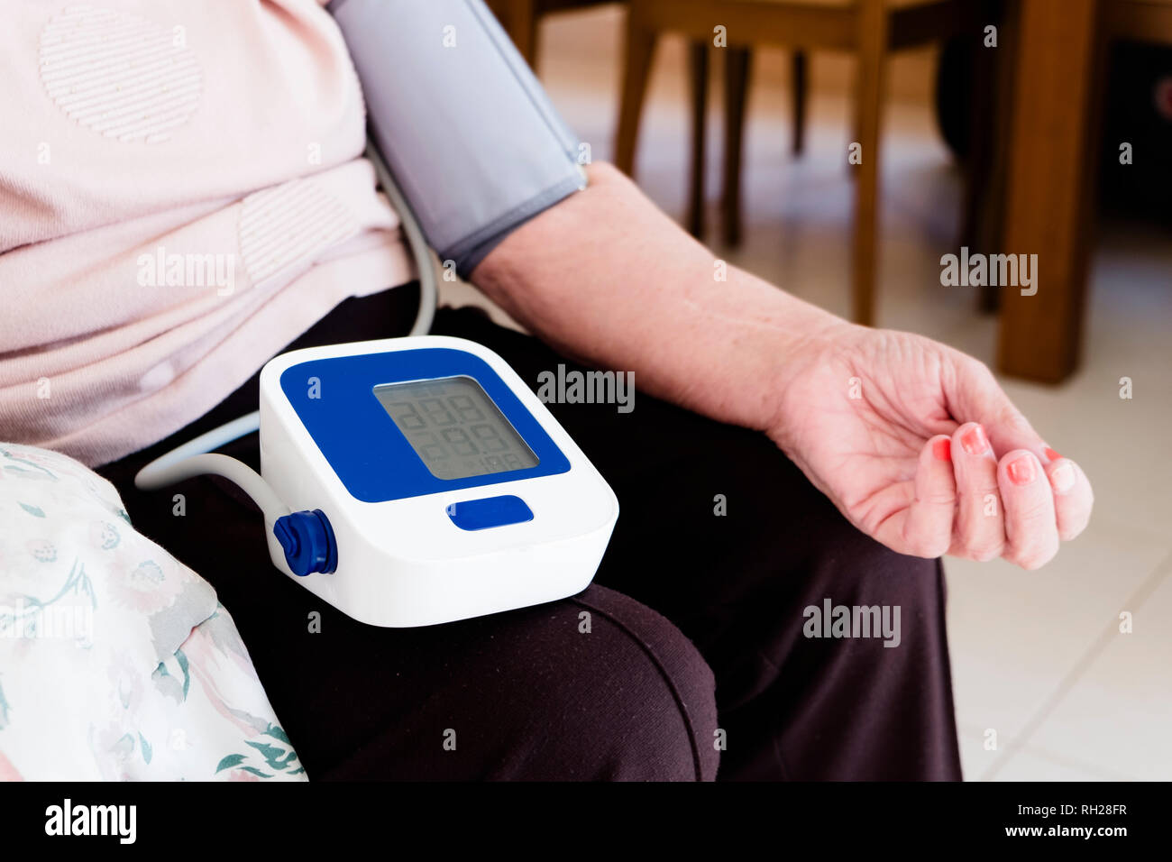 Primo piano di un senior donna caucasica con uno sfigmomanometro nel suo braccio, di misurare la sua pressione sanguigna, a casa sua o in una casa di cura Foto Stock