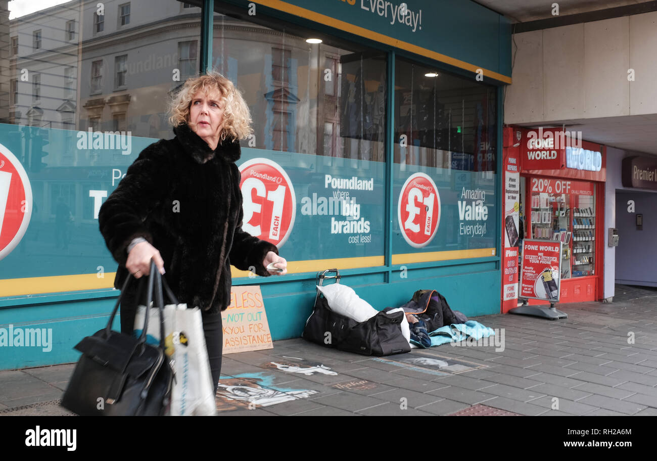 Sottolineato shopper femmina passa da un senzatetto camp al di fuori di un negozio Poundland in Brighton Foto Stock