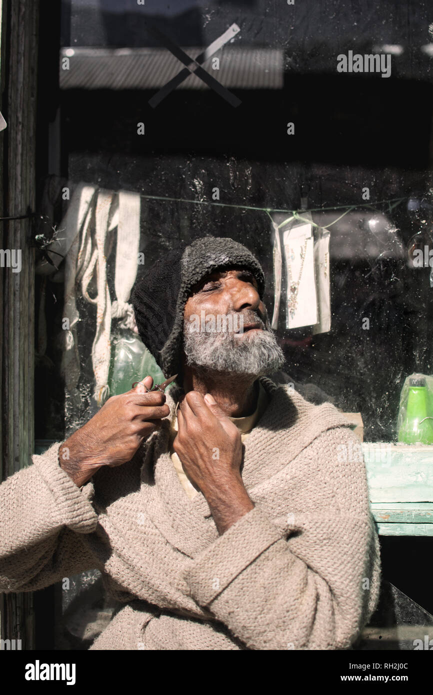 Un uomo anziano che taglia la barba con le forbici sulla strada nella valle del Neelum, Azad Kashmir, Pakistan Foto Stock
