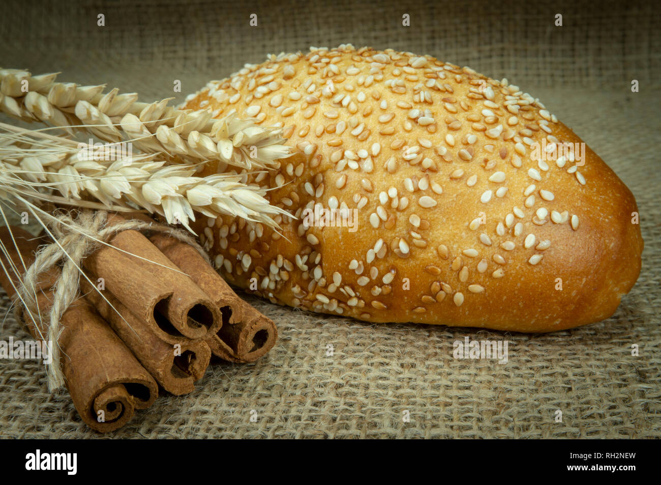 Singolo seme di sesamo bun, orecchio di grano maturo e fascio di stecche di cannella sul tessuto di iuta di superficie Foto Stock
