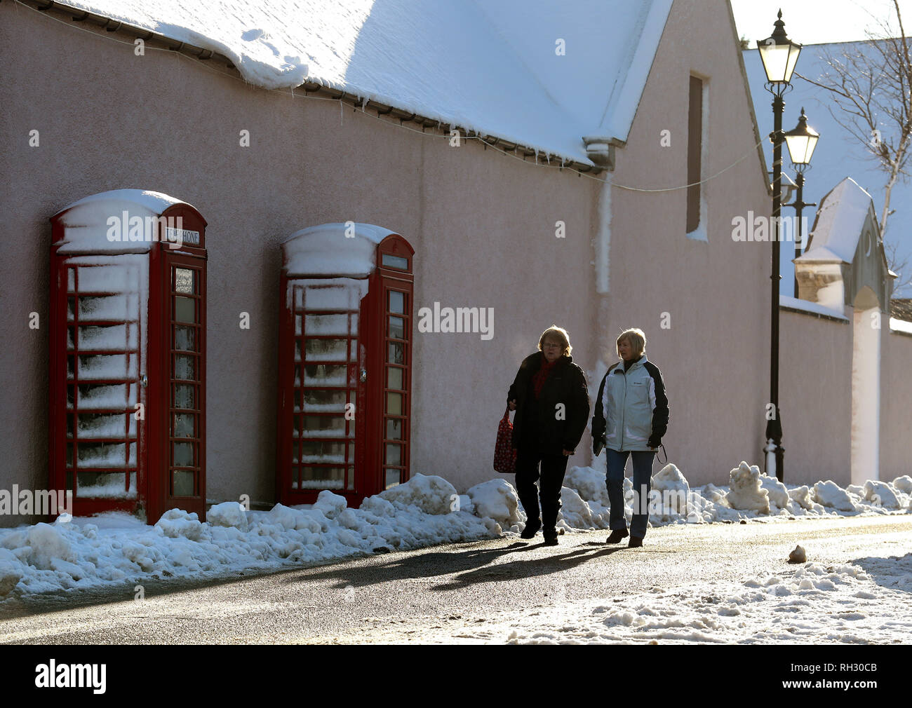 Le donne a piedi passato coperta di neve cabine telefoniche in Braemar nelle Highlands scozzesi dopo il villaggio era uno dei luoghi più freddi nel Regno Unito la notte scorsa come temperature è sceso di quasi -15C. Foto Stock