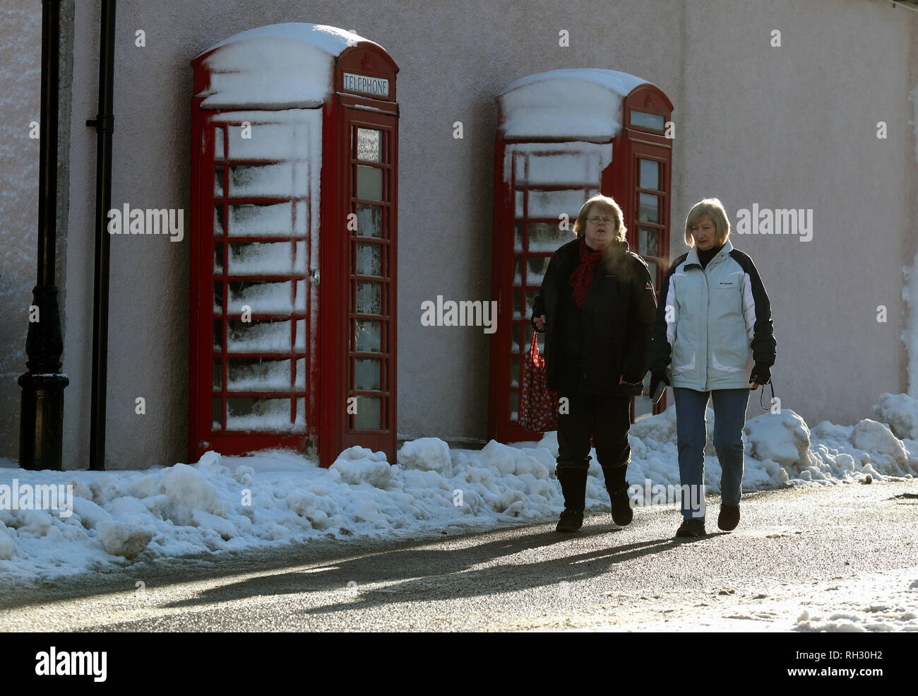 Le donne a piedi passato coperta di neve cabine telefoniche in Braemar nelle Highlands scozzesi dopo il villaggio era uno dei luoghi più freddi nel Regno Unito la notte scorsa come temperature è sceso di quasi -15C. Foto Stock