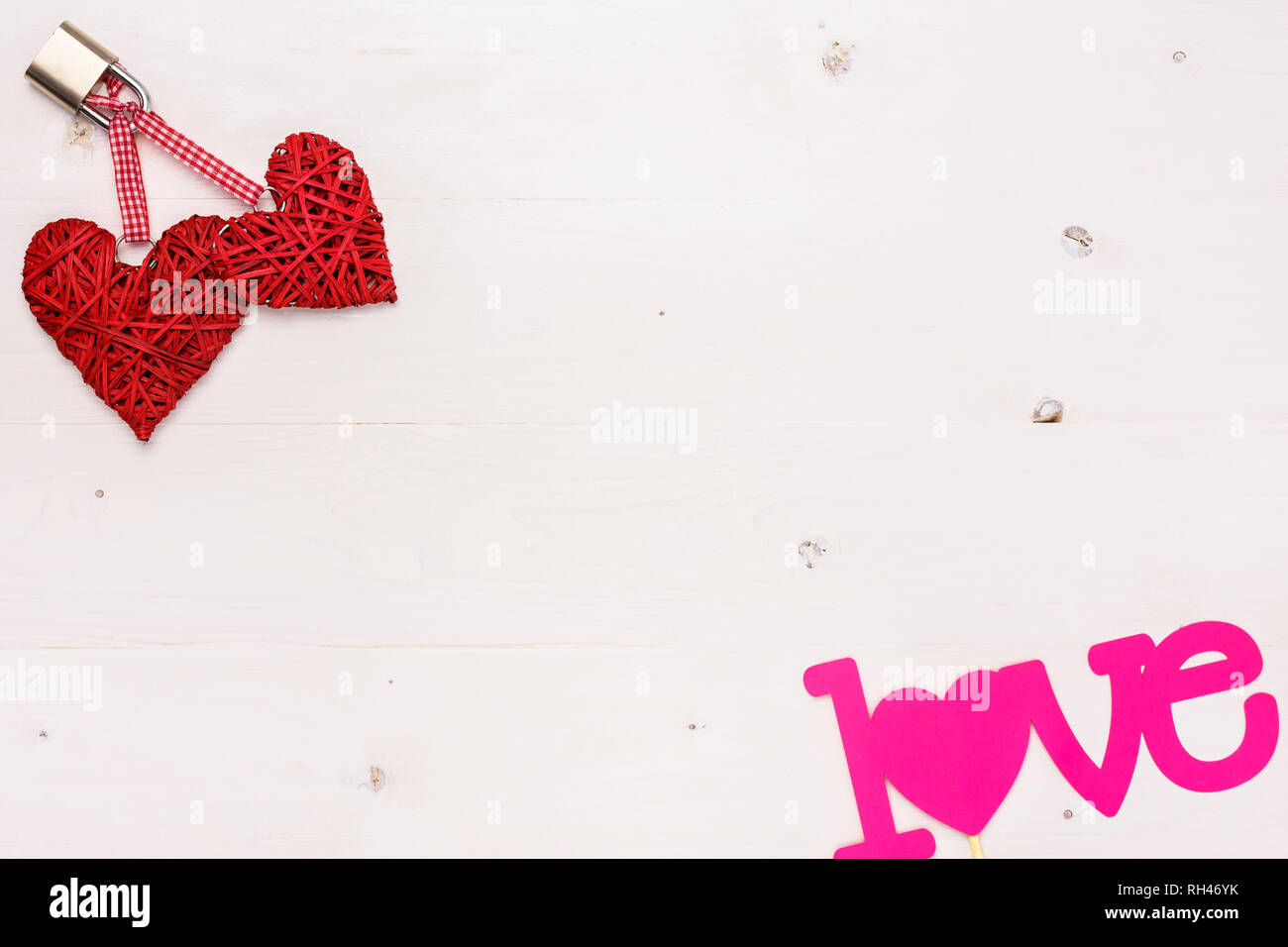Due cuori rossi bloccato con un lucchetto e un amore testo rosa su bianco tavola di legno. Valentines Day card concetto con copia spazio per il testo. Foto Stock
