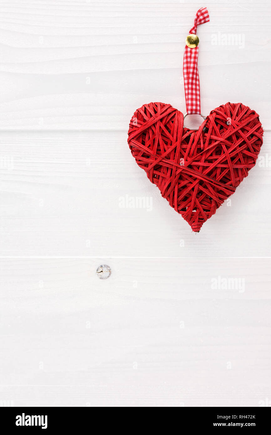 Cuore di vimini appesi a un bianco tavola di legno. Valentines Day card concetto con copia spazio per il testo. Foto Stock