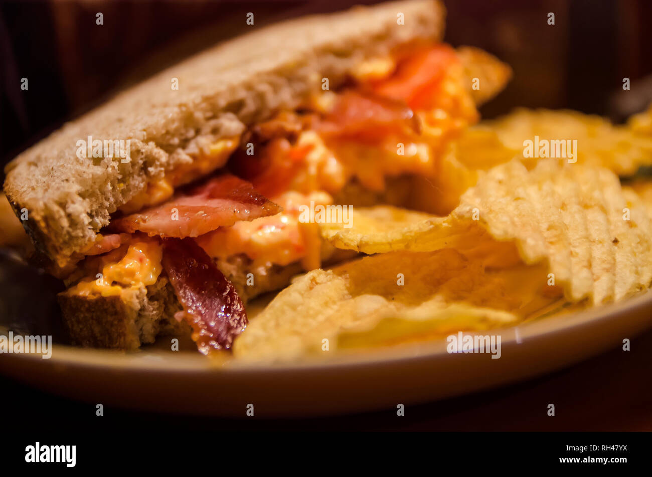 Un Southern-style pimiento panino al formaggio, viene servita su tutto il pane di grano, accentati con pancetta e fresca di pomodori a fette e servito con patate fritte. Foto Stock