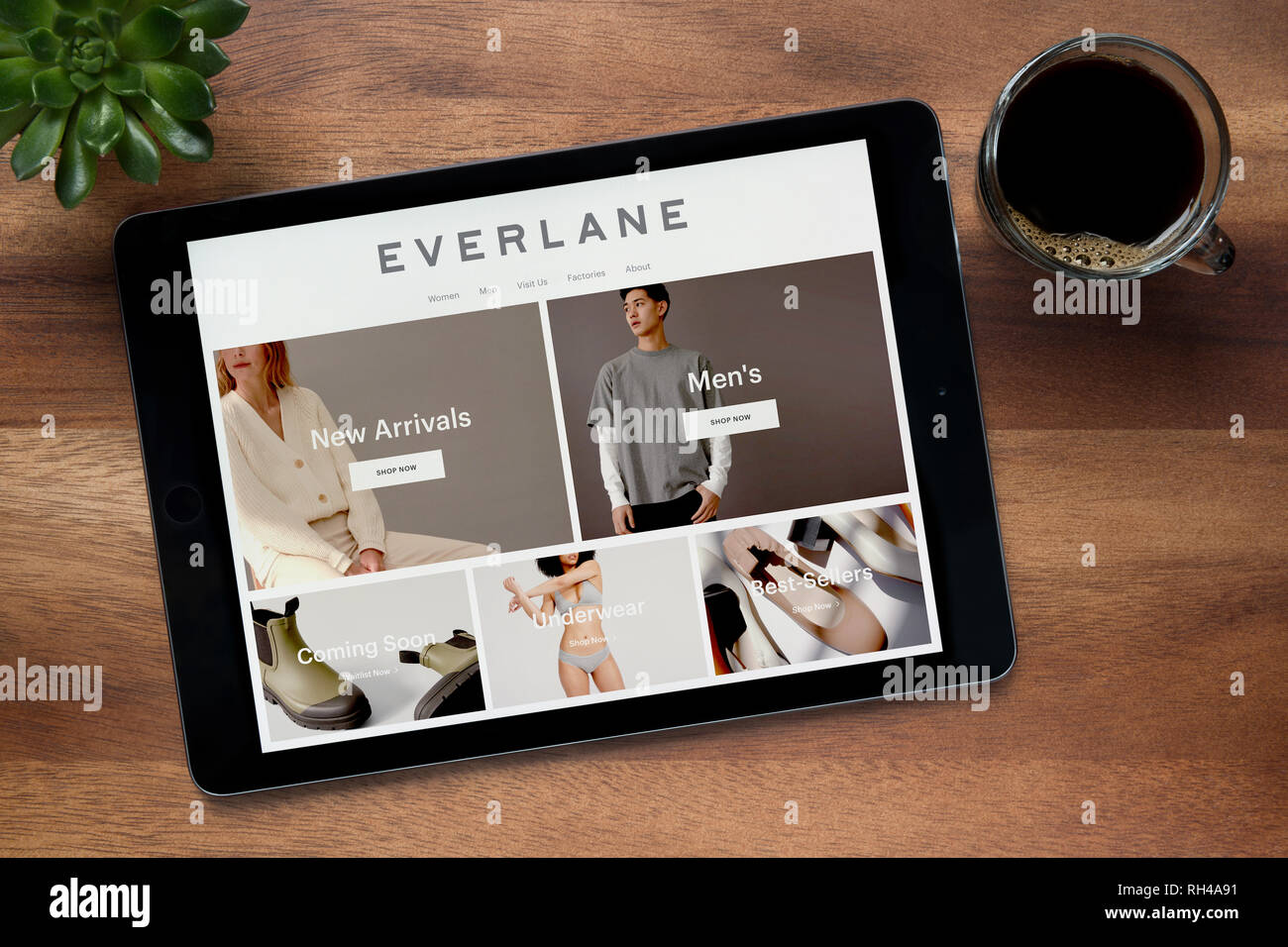 Il sito web di Everlane è visto su un tablet iPad, su di un tavolo di legno lungo con un caffè espresso e una pianta di casa (solo uso editoriale). Foto Stock