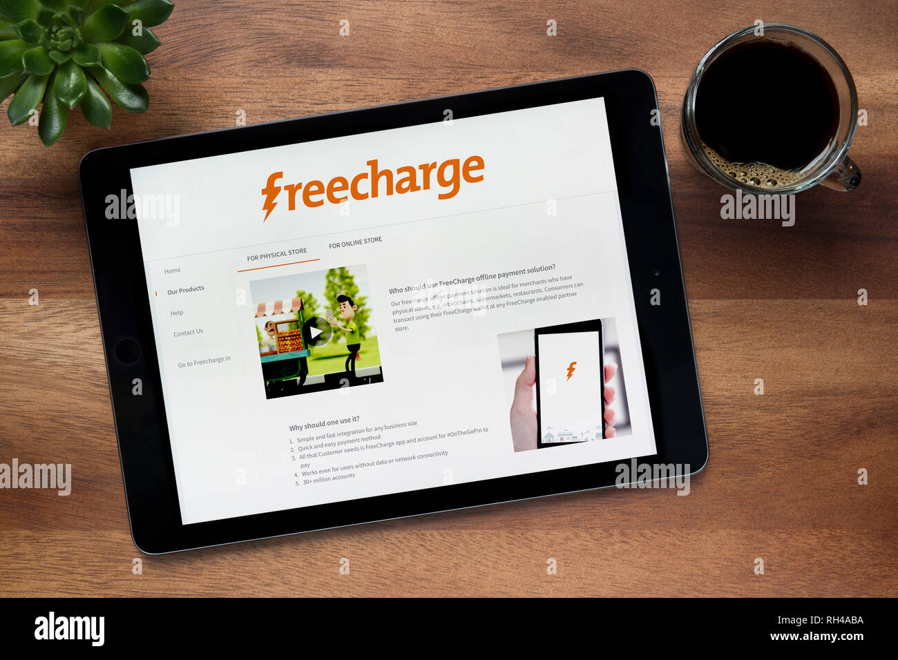 Il sito web di Freecharge è visto su un tablet iPad, su di un tavolo di legno lungo con un caffè espresso e una pianta di casa (solo uso editoriale). Foto Stock