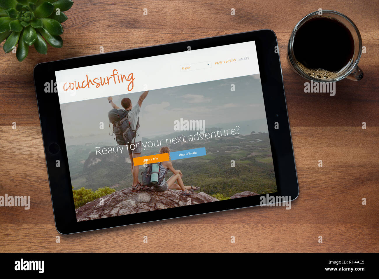 Il sito web di Couchsurfing è visto su un tablet iPad, su di un tavolo di legno lungo con un caffè espresso e una pianta di casa (solo uso editoriale). Foto Stock