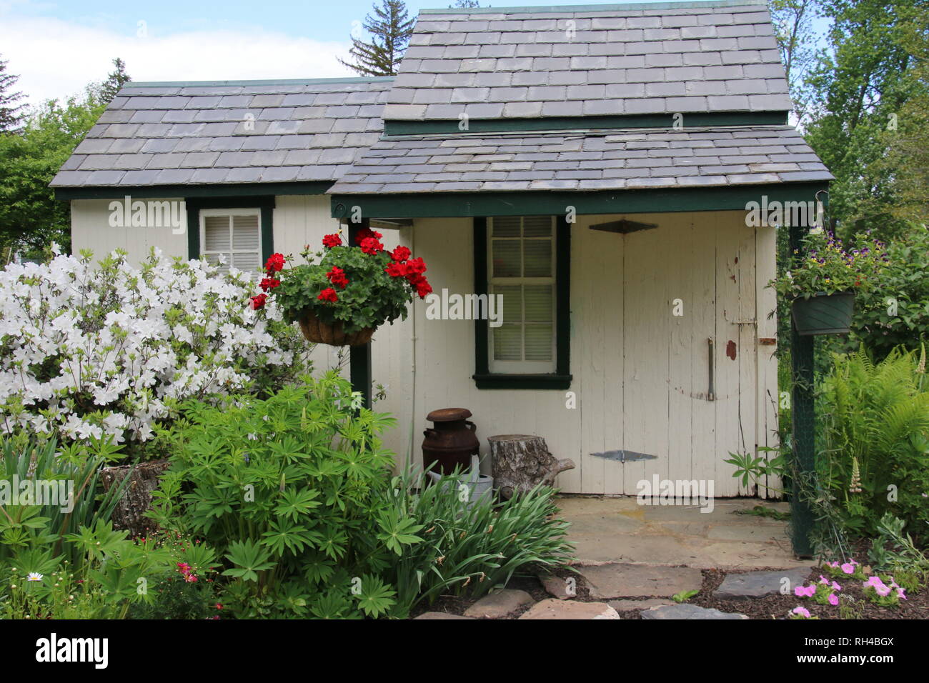 Questo piccolo cottage è circondato da piante e fiori. Foto Stock