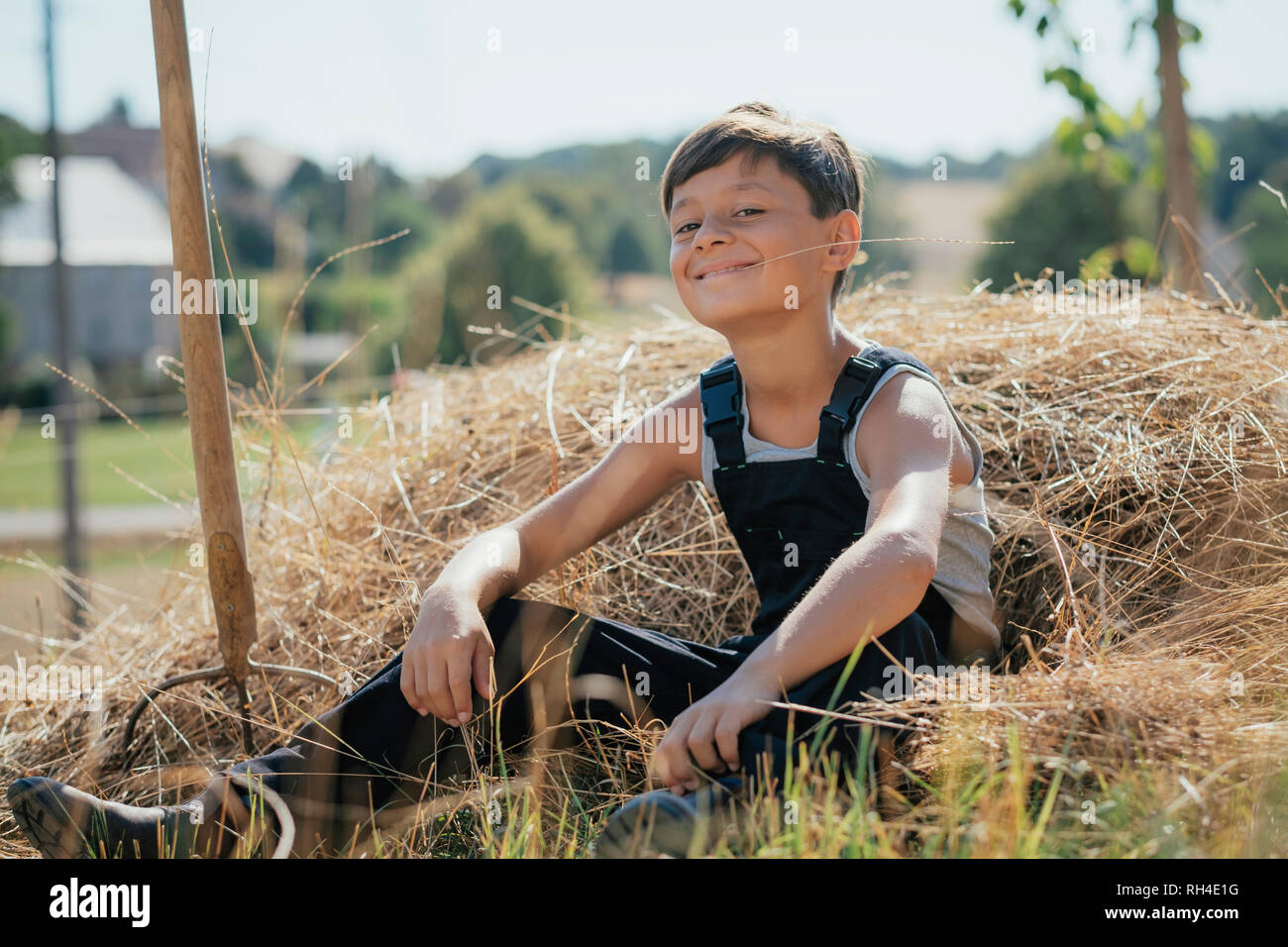 Ritratto fiducioso e sorridente ragazzo in tuta masticare fieno di sunny farm Foto Stock