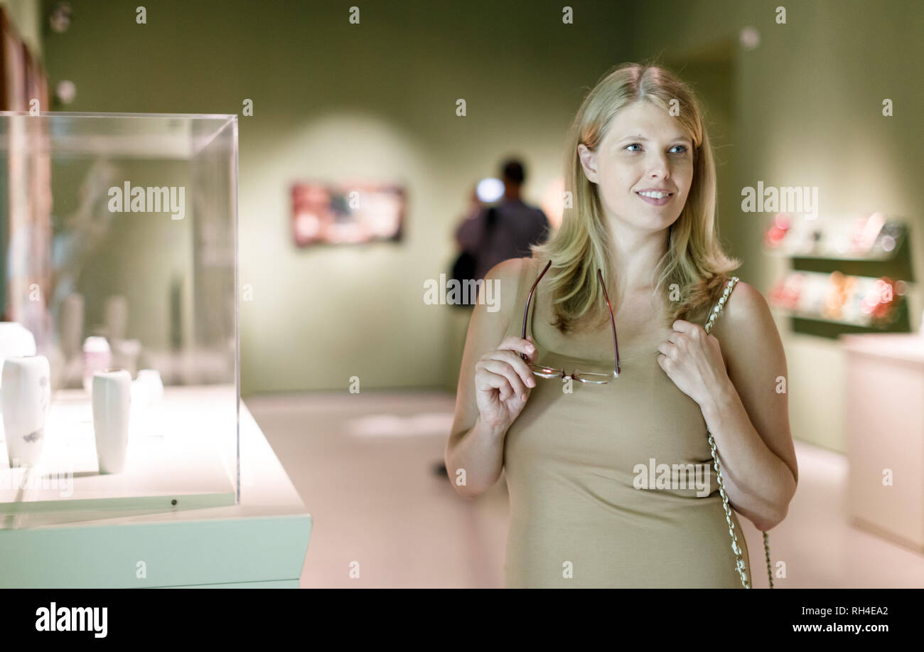 Donna positivo con gli occhiali visitando il museo storico e guardare vetrine con mostre Foto Stock