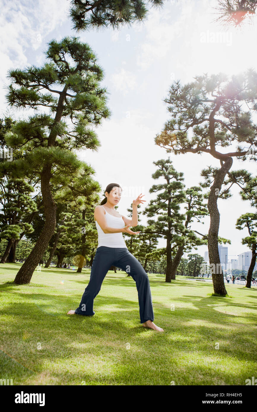 Donna pratica il tai chi nel soleggiato parco, Tokyo, Giappone Foto Stock