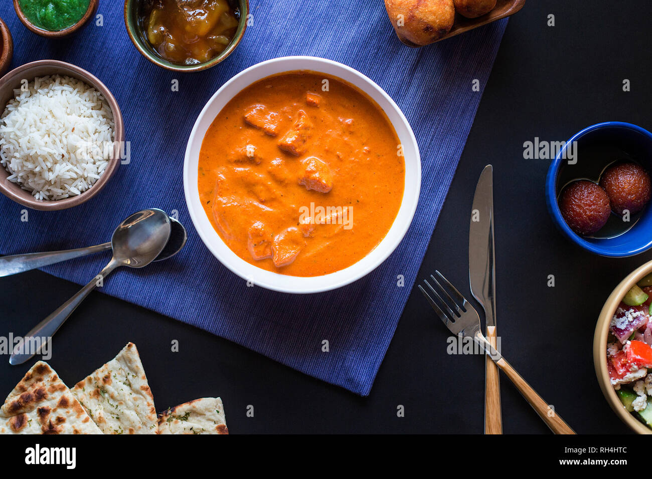 Vista aerea del cibo indiano, con pollo Tikka Masala, riso, chutney, Naan, e piatti laterali sulla biancheria blu. Foto Stock