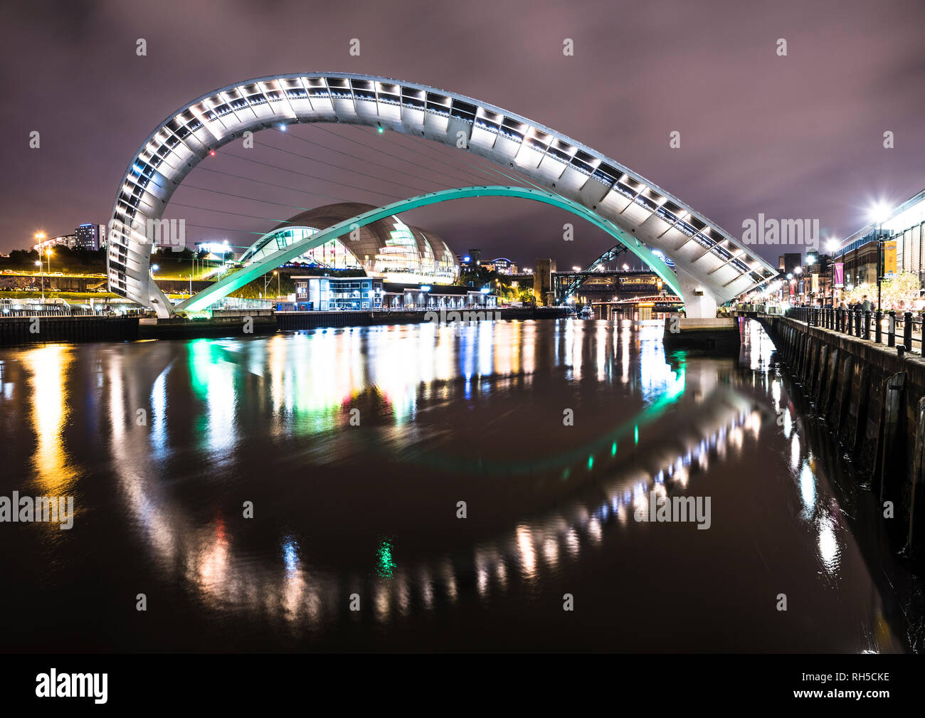 Notte foto guardando lungo il Fiume Tyne verso Gateshead Millennium Bridge con Tyne Bridge in background, Newcastle upon Tyne Foto Stock