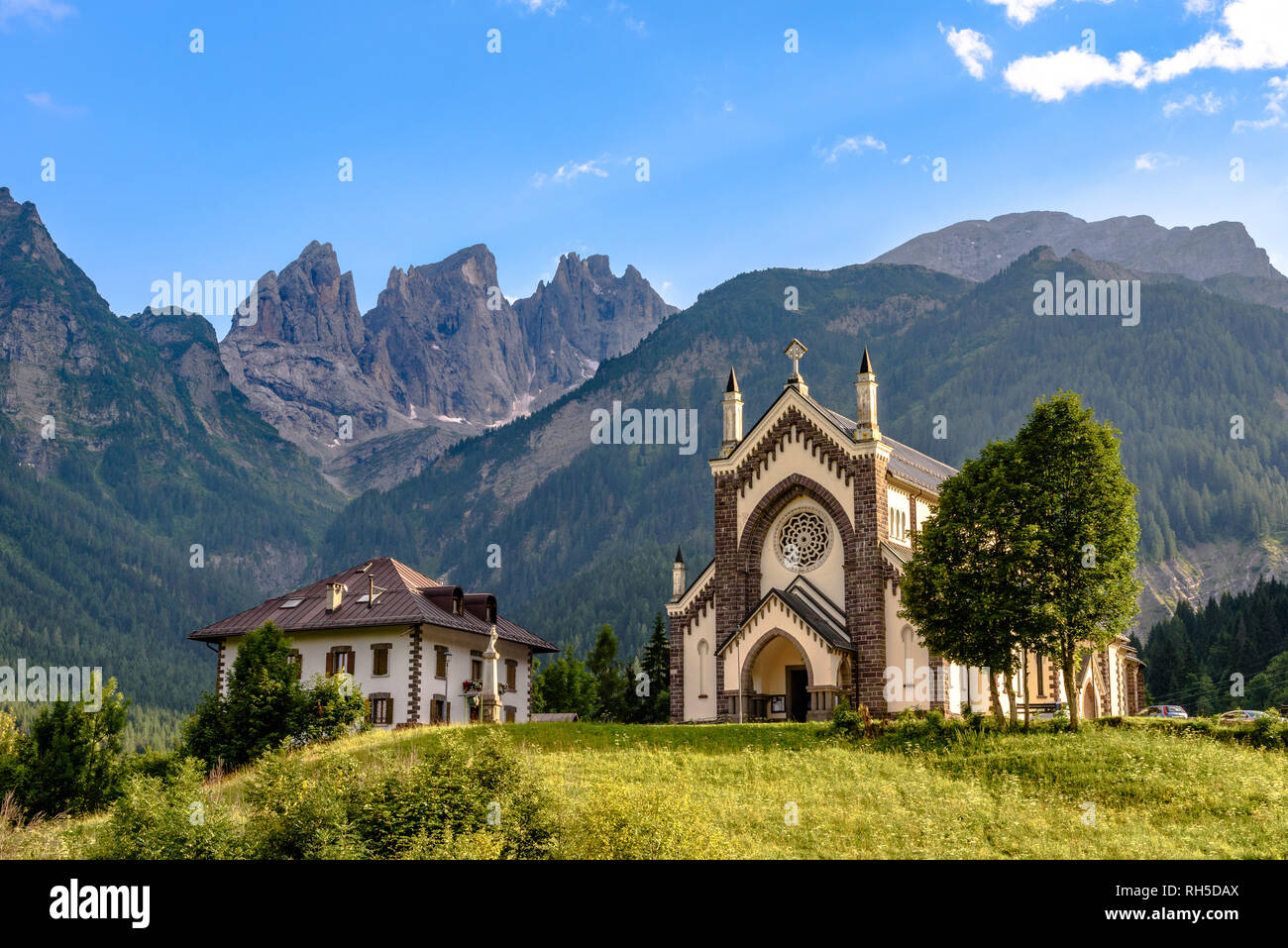 Il San Sebastian chiesa in Falcade su una soleggiata giornata estiva con le cime del gruppo della pala in background Foto Stock