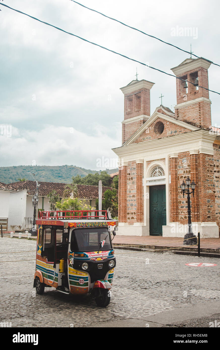 Verniciato colorato tuktuk si trova al di fuori della cappella di mattoni nella tipica cittadina colombiana di Santa Fe de Antioquia vicino a Medellín, in Colombia Foto Stock