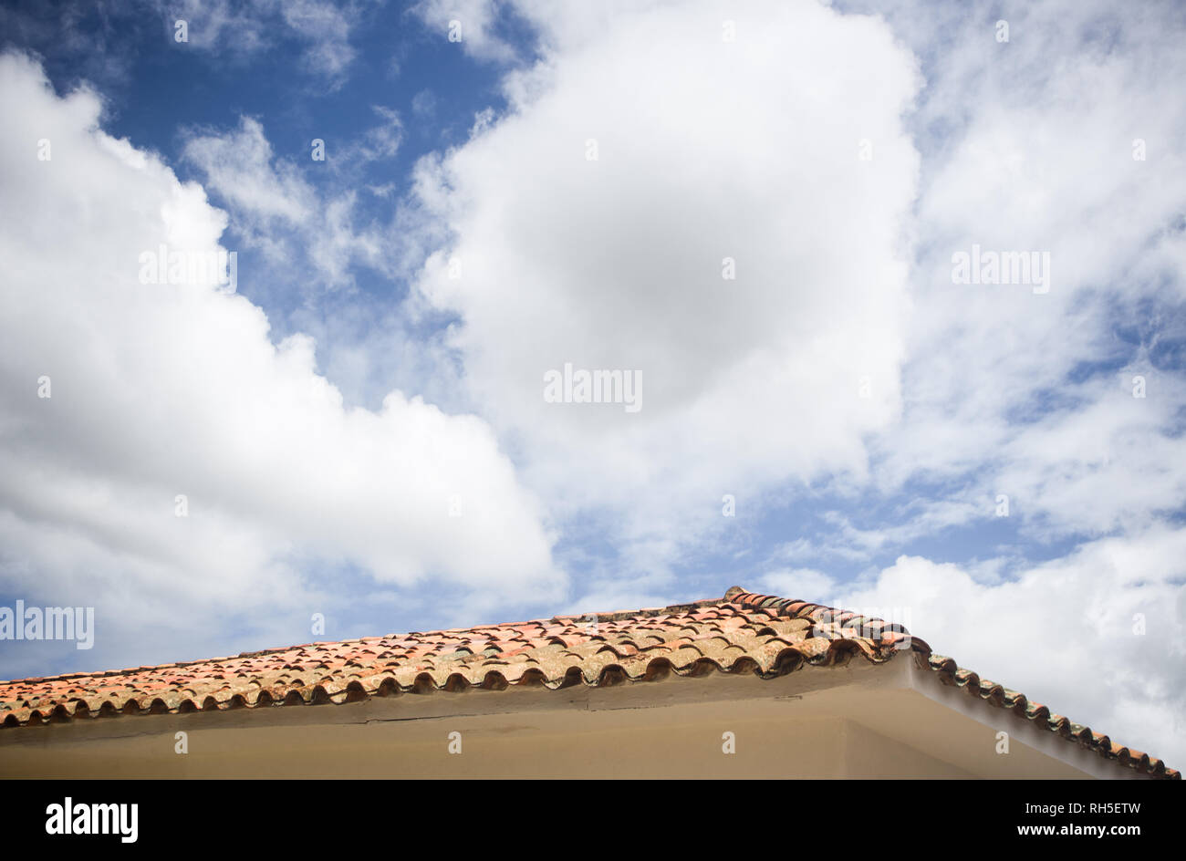 Nuvoloso blu cielo creando lo spazio negativo per copiare su un tipico in piastrelle di terracotta tetto di una casa bianca in Villa de Leyva, Colombia Foto Stock