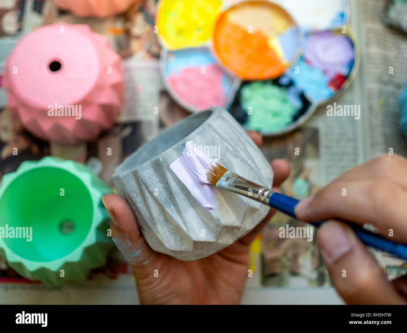 Pittura a mano pastel color porpora sul piccolo piantatrice di calcestruzzo con pennello blu. Colore acrilico dipinto su piccolo vaso geometrico. Foto Stock