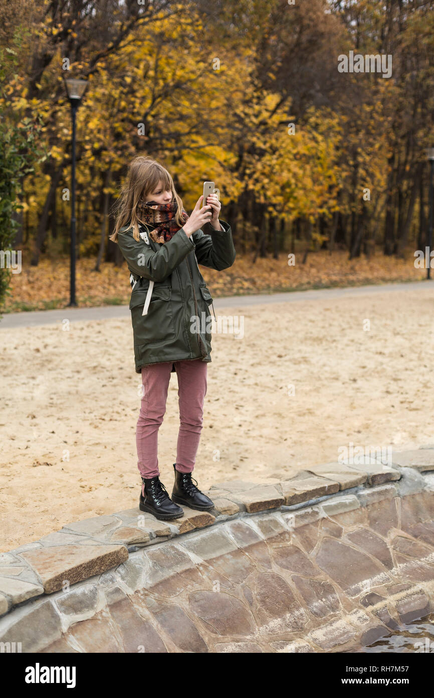 Tween girl tramite telefono cellulare dotato di fotocamera digitale in autunno park Foto Stock