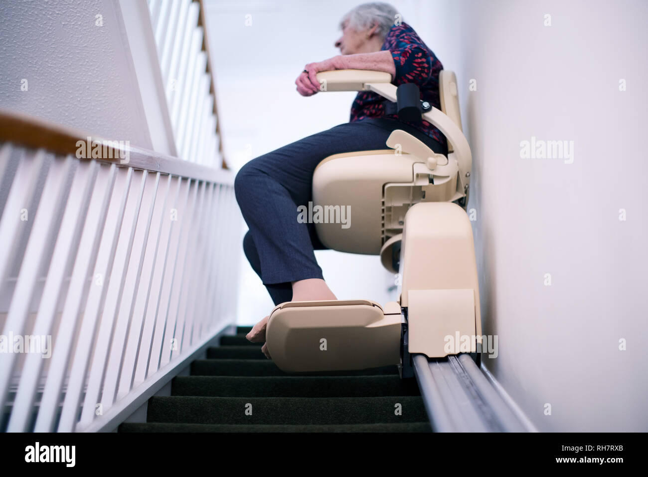 Senior donna seduta sul sollevamento Scale a casa per aiutare la mobilità Foto Stock
