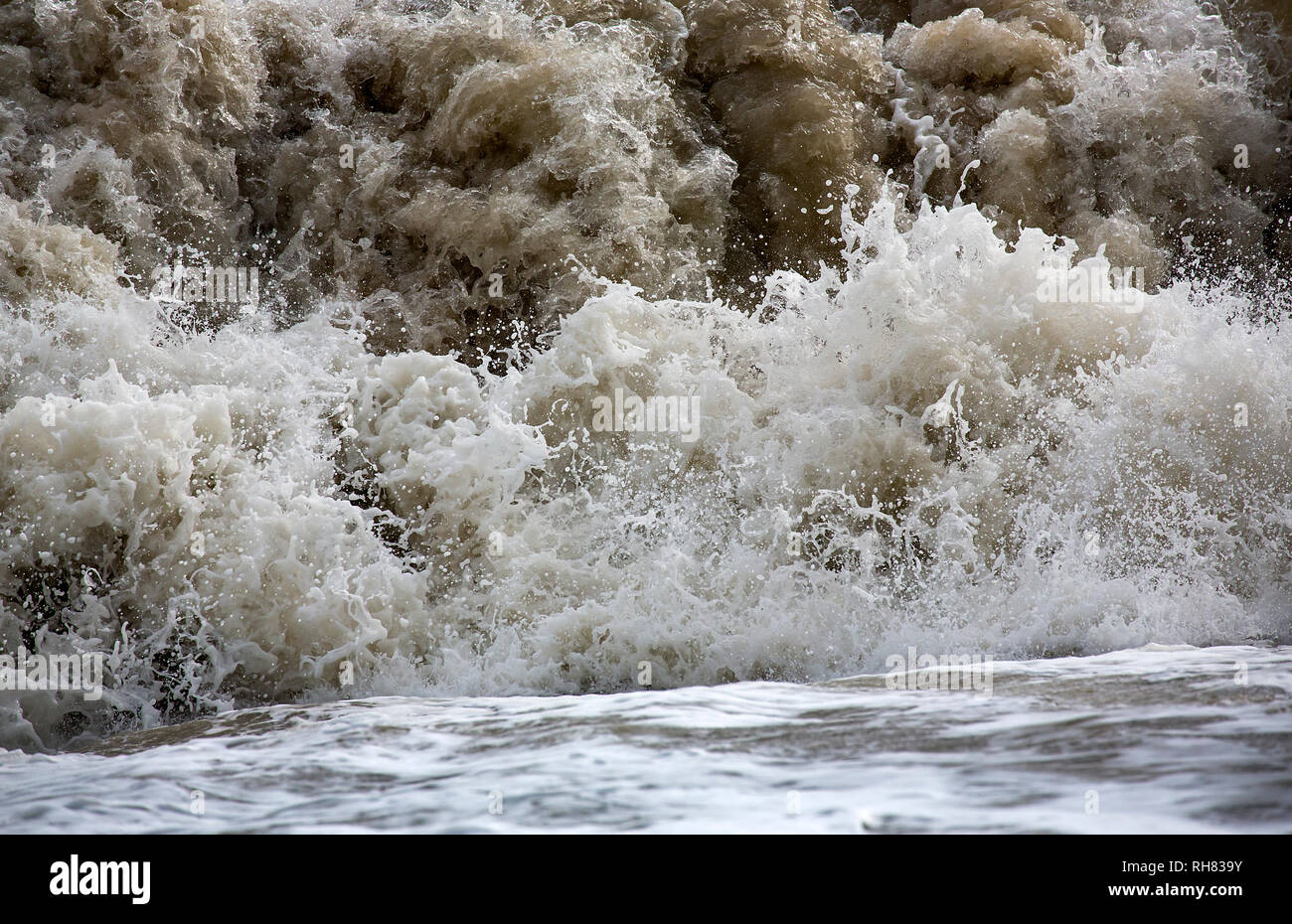 Sea Wave schiantarsi su una spiaggia in un giorno di tempesta in Inghilterra con spruzzo di goccioline e che rappresentano la forza e il movimento. Foto Stock