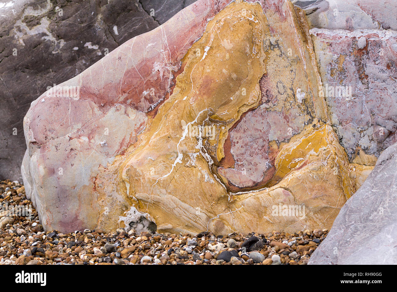 Roccia di colore rosso giallo grigio con striature sulle linee una delle  molte rocce sulla spiaggia Goring Worthing Regno Unito. Questo ha colori  vivaci su un letto di ghiaia Foto stock -