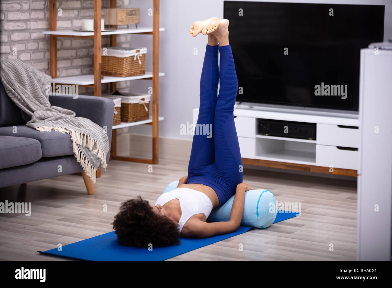 Una giovane donna facendo gamba in alto esercizio sul materassino yoga nella stanza vivente Foto Stock