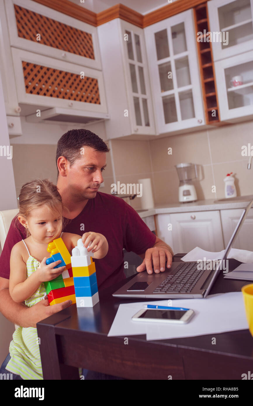 Il Multitasking giovane padre è servizio di baby sitter e lavorare a casa. Foto Stock