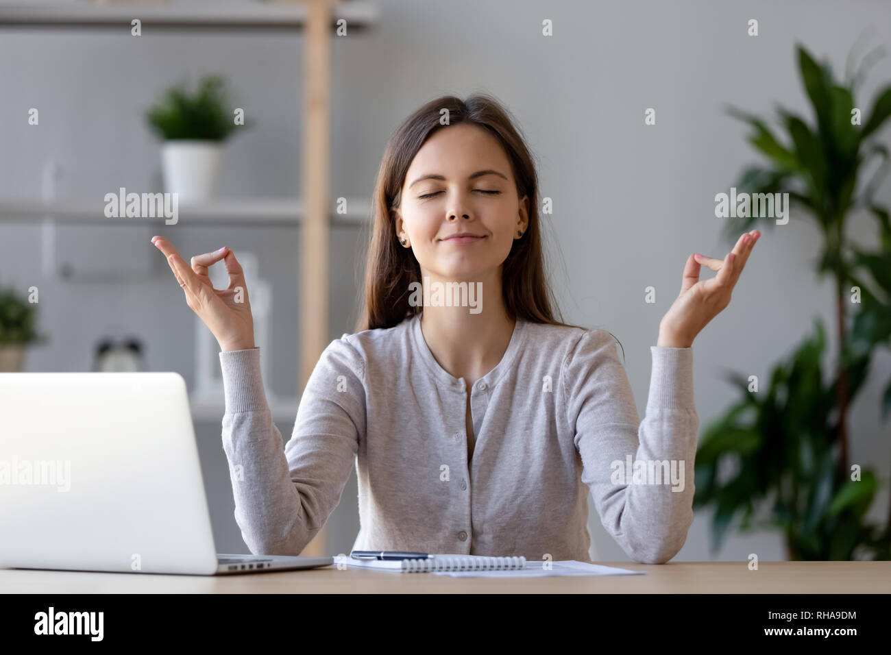 Calma giovane donna prendendo break facendo esercizi yoga al lavoro Foto Stock