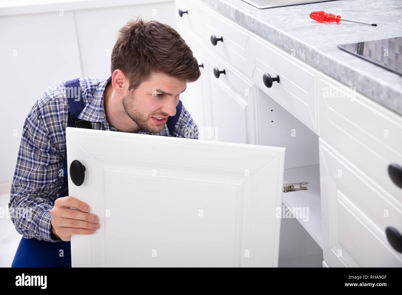Sorridente tuttofare il montaggio di una nuova porta al di sotto del piano di lavoro della cucina Foto Stock