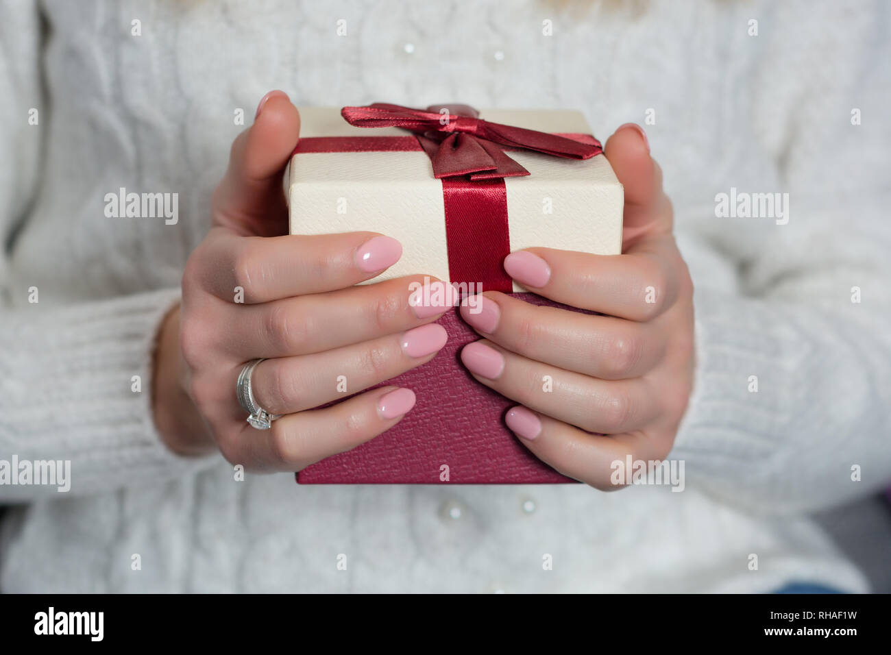 Giovani mani femminili con baby colore rosa chiodi polacco su dita azienda confezione regalo rossa. Manicure e il giorno di San Valentino del concetto. Close up, il fuoco selettivo Foto Stock